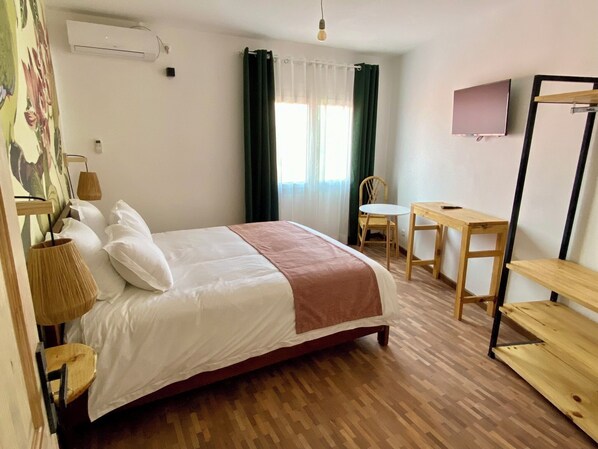 A hotel room with a bed, a desk, a chair, a TV, and a window with curtains. - Hôtel Escale (Antananarivo)