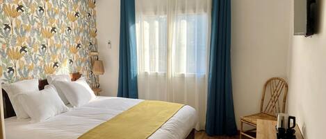 A hotel room with a bed, a desk, a chair, a television, and a window with curtains.