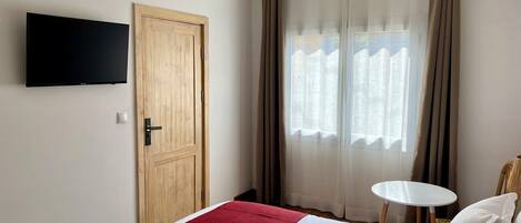 Una habitación de hotel con una cama, un televisor montado en la pared, una puerta y una ventana con cortinas.