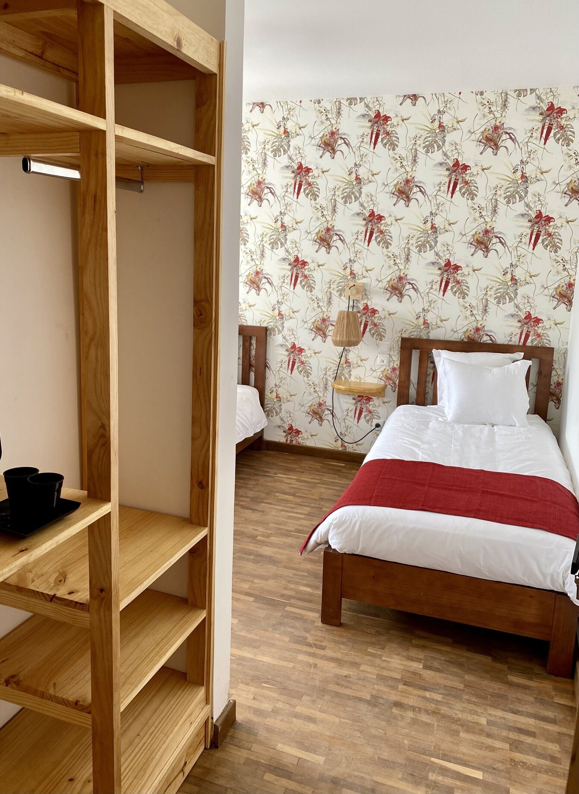 Un dormitorio con una cama de madera, una manta roja, un armario de madera y un papel tapiz con motivos florales.