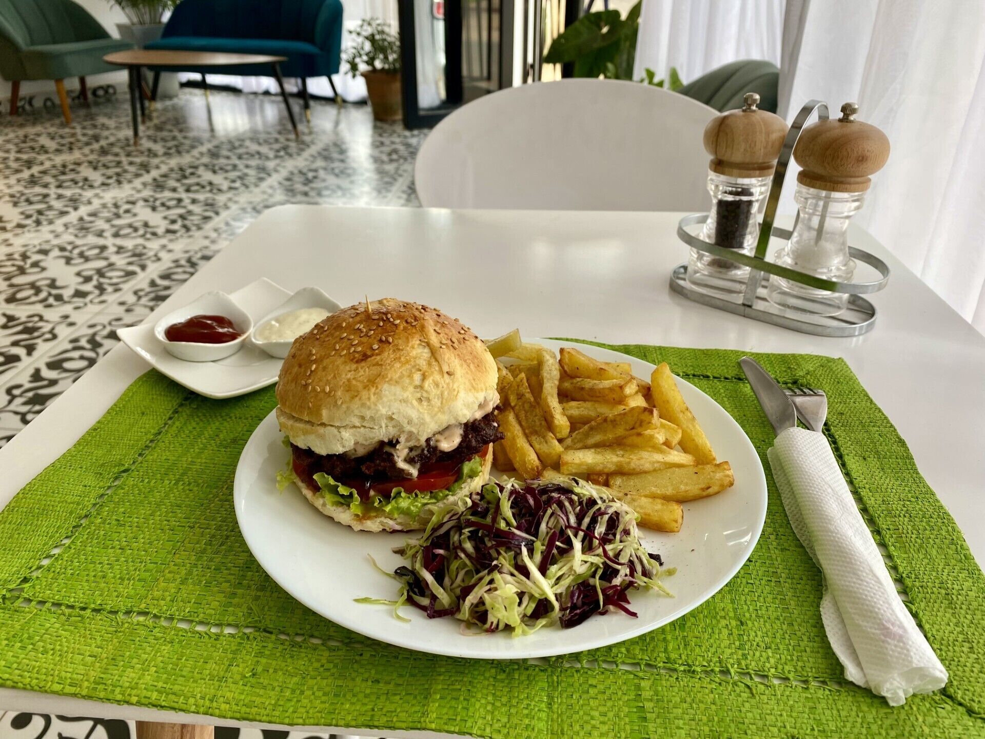 Un plato con una hamburguesa, papas fritas y ensalada de col sobre una mesa con camino de mesa verde.