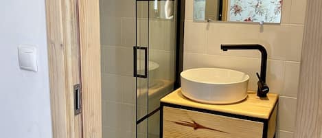 Un baño con cabina de ducha de vidrio, tocador de madera con lavabo blanco y espejo con motivos florales.