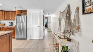 A kitchen with wooden cabinets, a stainless steel refrigerator, a white door, and a hallway with a white wall and decorative netting.
