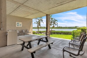 Un patio al aire libre con una mesa y sillas de hormigón, un mueble blanco pequeño y un cuadro en la pared.