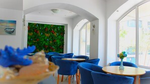 A modern interior with blue chairs and tables, a green wall with flowers, and large windows. - Briza Boutique Mamaia (Constanta)