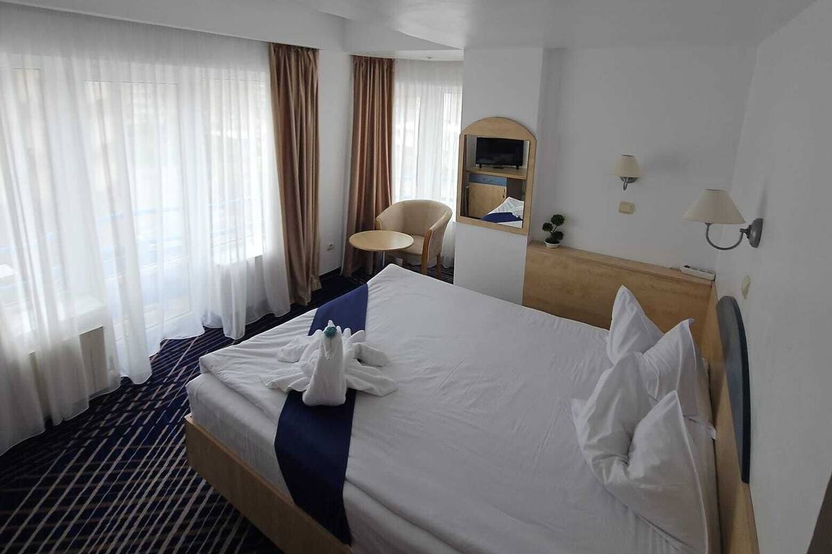 Ein Hotelzimmer mit einem großen Bett, einem Schreibtisch, einem Sessel und einem Fernseher auf einem Tisch.