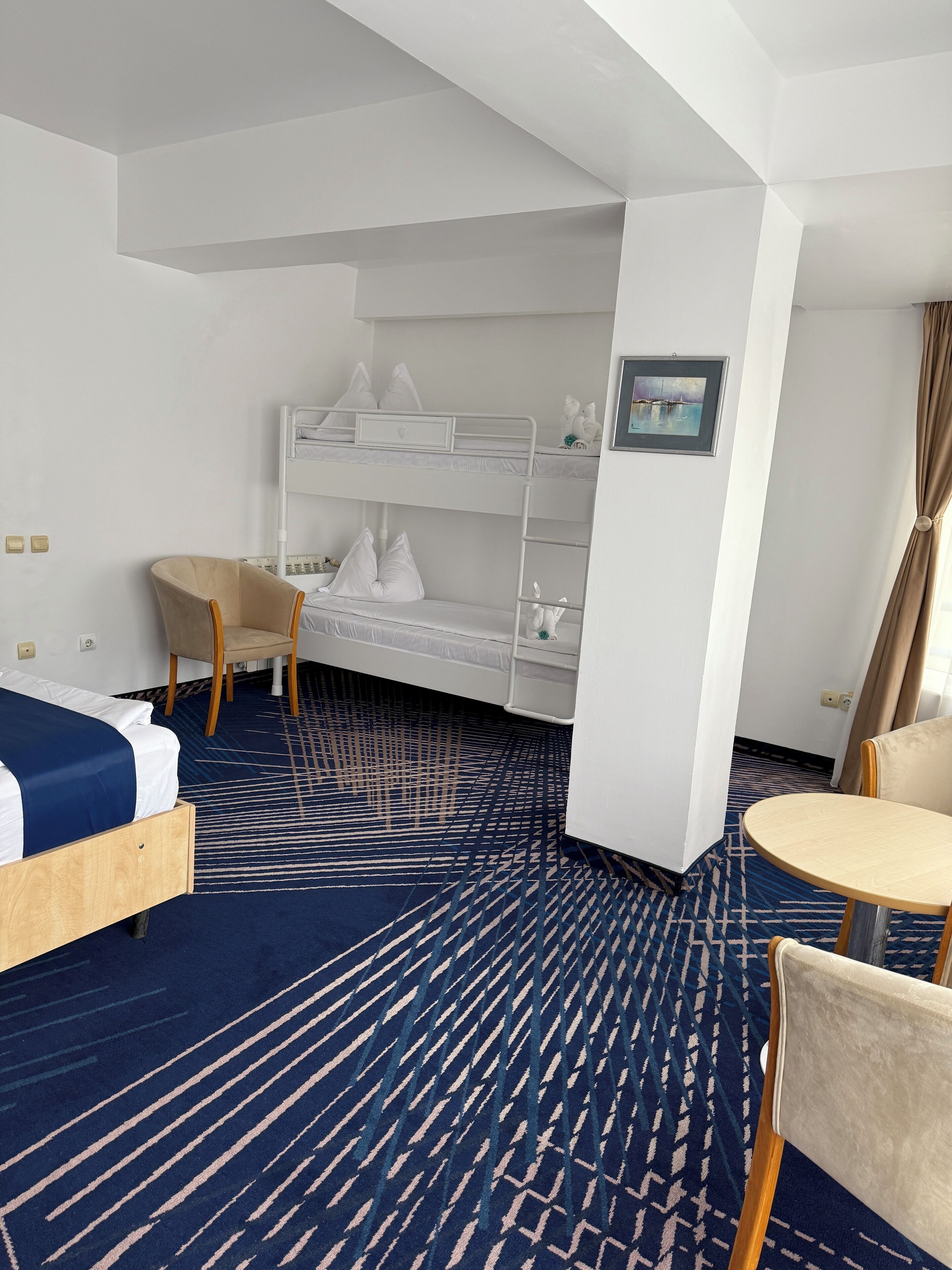 Habitación de hotel con literas, una cama individual, una silla, una mesita y una alfombra estampada.