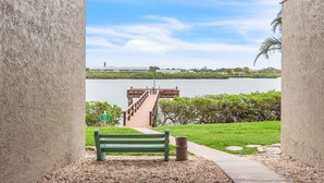 A bench and a pathway leading to a dock over water. - Pelican's Perch - Expansive Condo with Water Views, Pool-Across from Beach (Indian Shores)