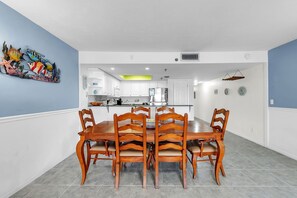Zona pranzo con tavolo e sedie in legno, una cucina sullo sfondo e un elemento decorativo a parete.