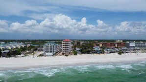 A beachfront hotel with multiple buildings, including a prominent red-roofed tower, situated along a sandy beach with ocean waves. - Pelican's Perch - Expansive Condo with Water Views, Pool-Across from Beach (Indian Shores)