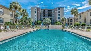 Une piscine entourée d’immeubles d’appartements, avec des chaises longues et des palmiers.