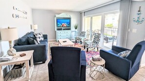A living room with a sofa, armchairs, a coffee table, and a TV. There is a window with a view of the outside. - Coastal Charm at Sea Club #13-Pool View and Fishing Dock (Indian Shores)