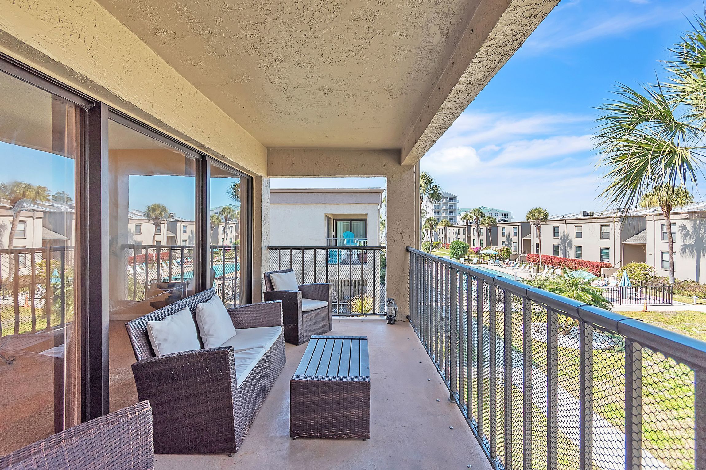 A balcony with wicker furniture, a view of neighboring buildings, and a clear sky.