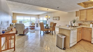 A spacious kitchen with a dining area, featuring a dishwasher, wooden cabinets, and a large window. - Manatee Zone,SeaClub #405~Corner unit with incredible water front views (Indian Shores)