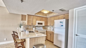 A kitchen with wooden cabinets, a microwave, an oven, a refrigerator, and a sink. - Manatee Zone,SeaClub #405~Corner unit with incredible water front views (Indian Shores)