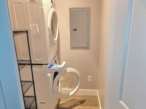 A laundry room with stacked washers and dryers, a utility door, and a metal shelf unit.
