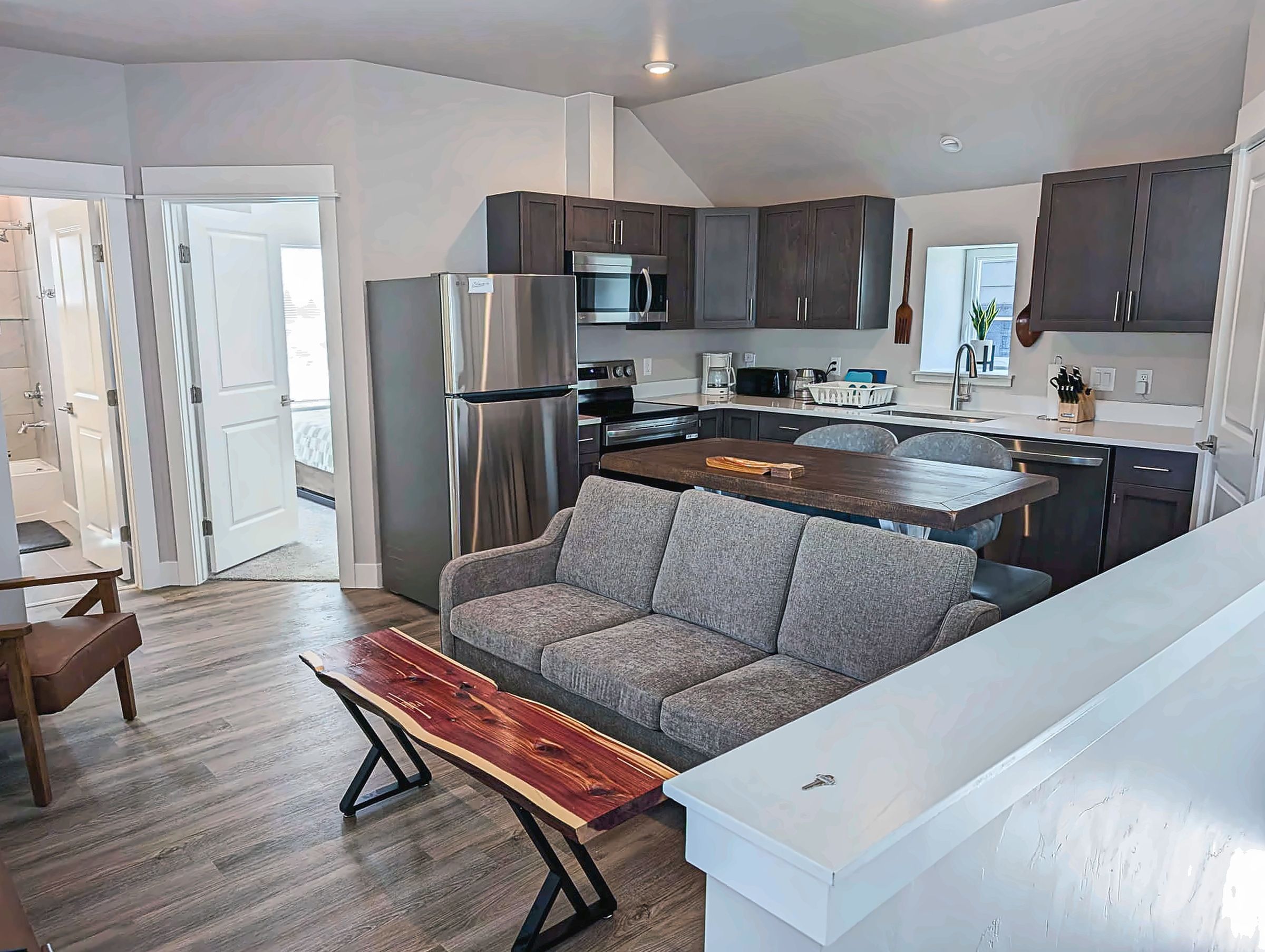 A modern kitchen with dark cabinets, stainless steel appliances, and a grey sofa in the living area.