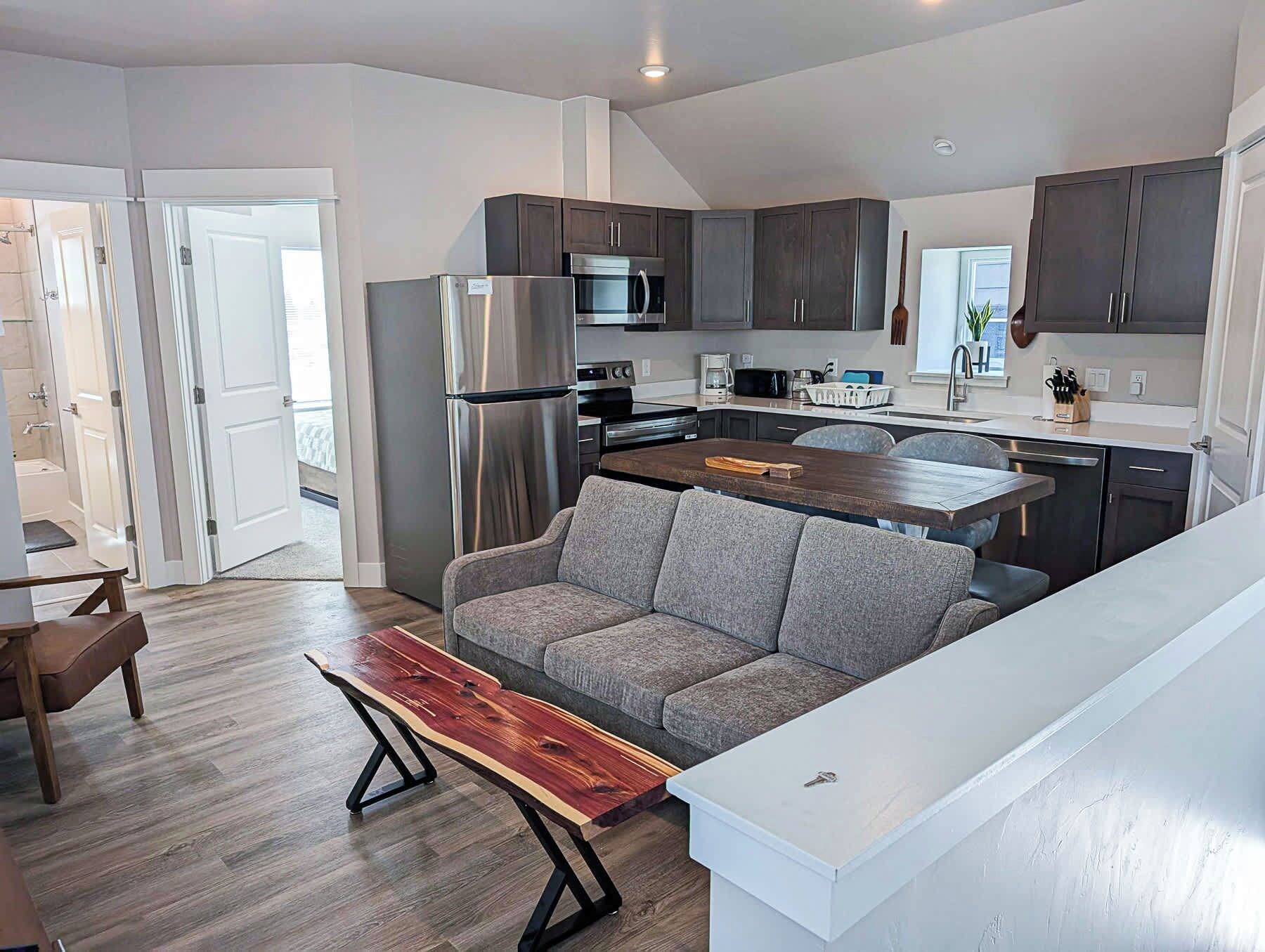A modern kitchen with dark cabinets, stainless steel appliances, and a grey sofa.