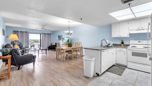 Una sala de estar moderna con sofá, mesa de comedor y área de cocina con armarios y electrodomésticos blancos.