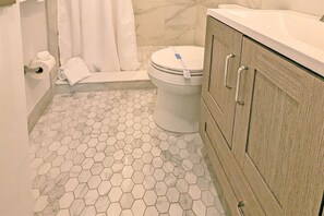 Bathroom features a hexagonal tile floor, a toilet, a towel on a bench, and a cabinet with metal handles.