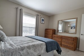 Relax in this serene bedroom with a large bed, wicker console table, and mirror.
