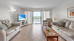 A modern living room with two leather sofas, a wooden coffee table, a flat-screen TV, and a balcony with a view. - Isle Be Back,SeaClub #402~Water View, Pool,Fishing (Indian Shores)