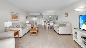 A spacious living room with a sofa set, a coffee table, and a TV stand. - Isle Be Back,SeaClub #402~Water View, Pool,Fishing (Indian Shores)