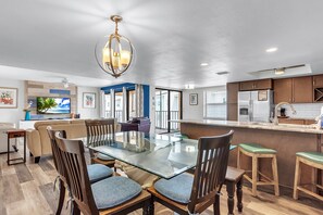 A modern kitchen with a central island, bar stools, and a dining table with chairs. - Coral Reef Retreat, SeaClub #44~Pool, Fishing (Indian Shores)