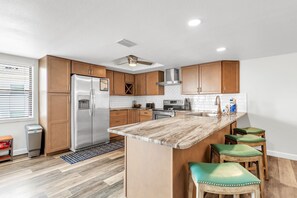 A modern kitchen with wooden cabinets, stainless steel appliances, a marble countertop, and a ceiling fan. - Coral Reef Retreat, SeaClub #44~Pool, Fishing (Indian Shores)