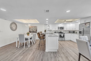 Una cocina moderna con armarios blancos, una isla central y una zona de comedor con mesa y sillas.
