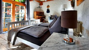 A bedroom with a bed, a nightstand, a lamp, a guitar, and a view of the outside.
