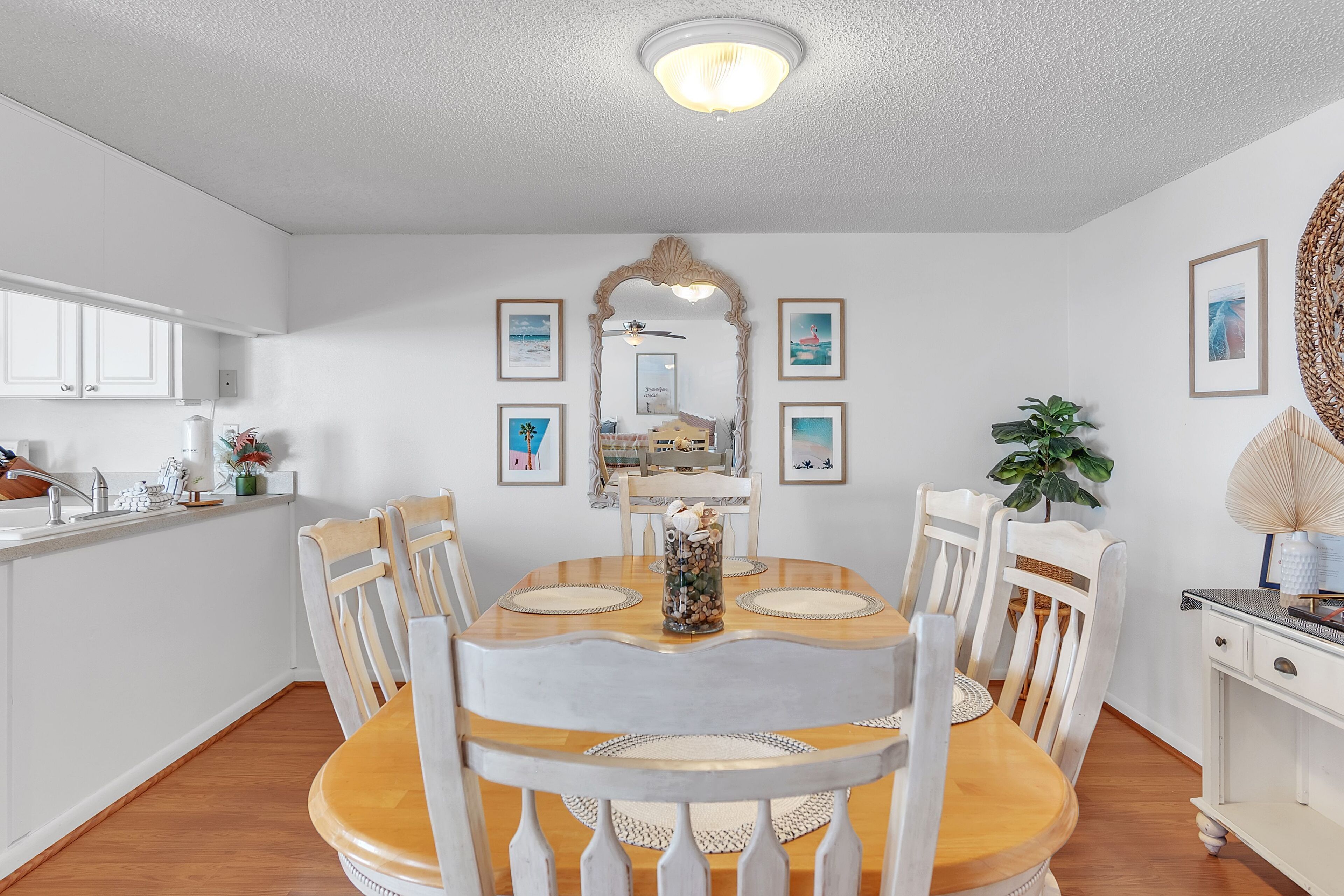 A dining area with a wooden table, white chairs, and a decorative mirror above.