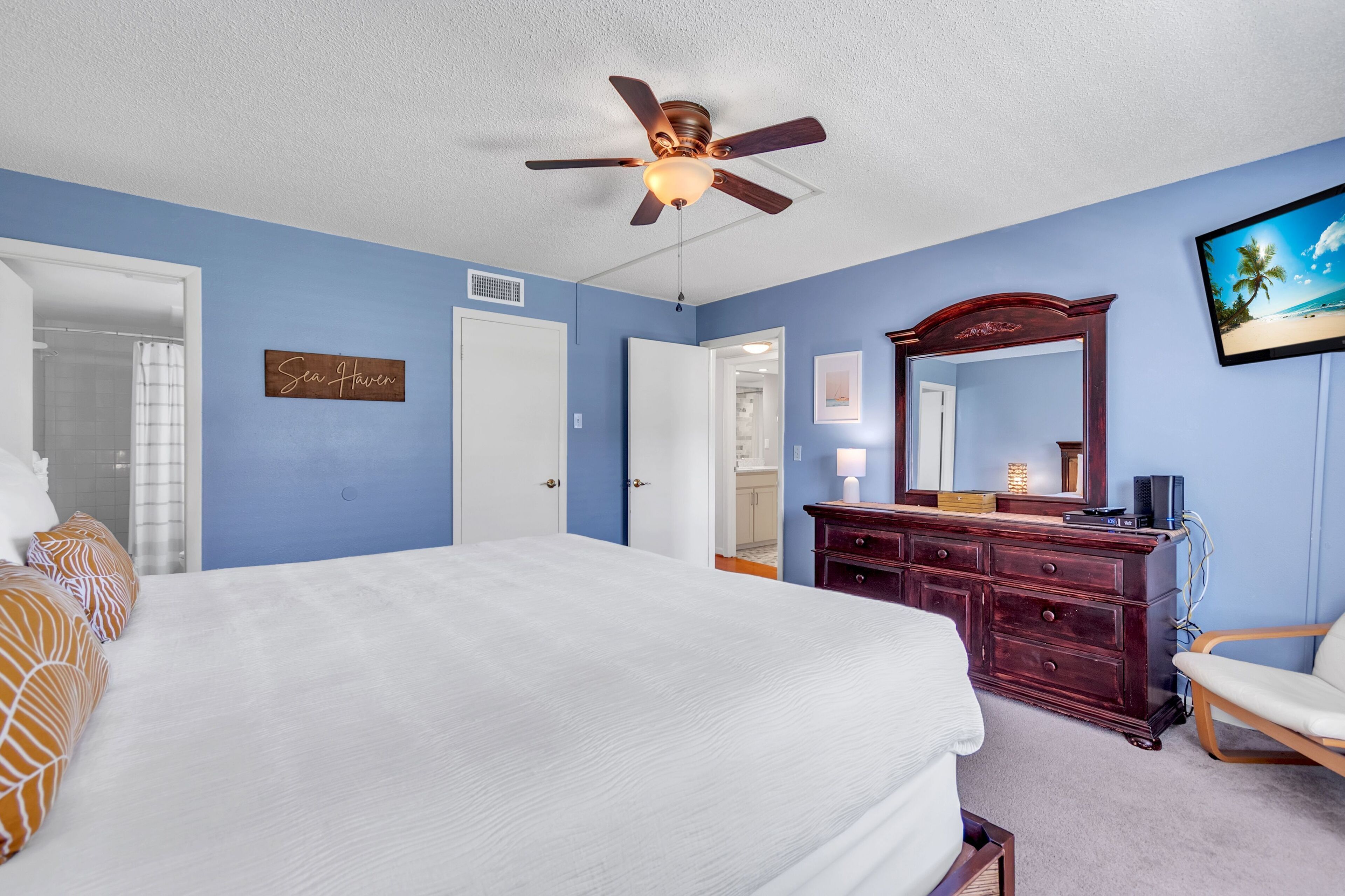 A bedroom with a bed, a dresser, a mirror, and a ceiling fan.