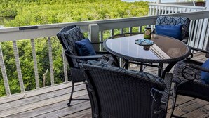 A deck with wicker furniture and a glass table, overlooking a water body and greenery.