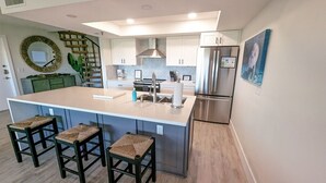 A modern kitchen with a large island, bar stools, stainless steel appliances, and a decorative mirror.