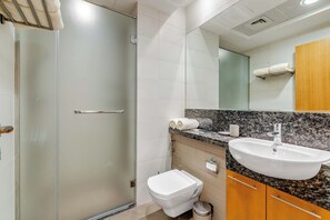 Et moderne badeværelse med et glasbadeværelsesafskærmning, et hvidt toilet, en vask med skiferplade og træskabe.