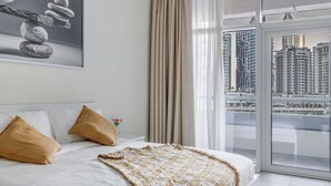 Une chambre d’hôtel moderne avec un grand lit, des rideaux de couleur beige et une vue sur la ville grâce à de grandes fenêtres du sol au plafond.