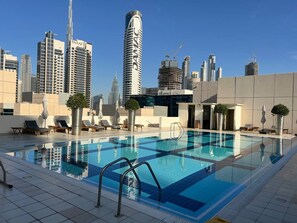 A rooftop pool with city views, lounge chairs, and potted plants. - Knokey Bay Square (Dubai)
