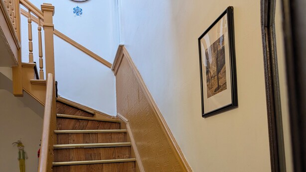 A wooden staircase with a handrail, a wall clock, and a framed picture.