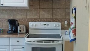A compact kitchen with white cabinets, a stove, a toaster, and a coffee maker.