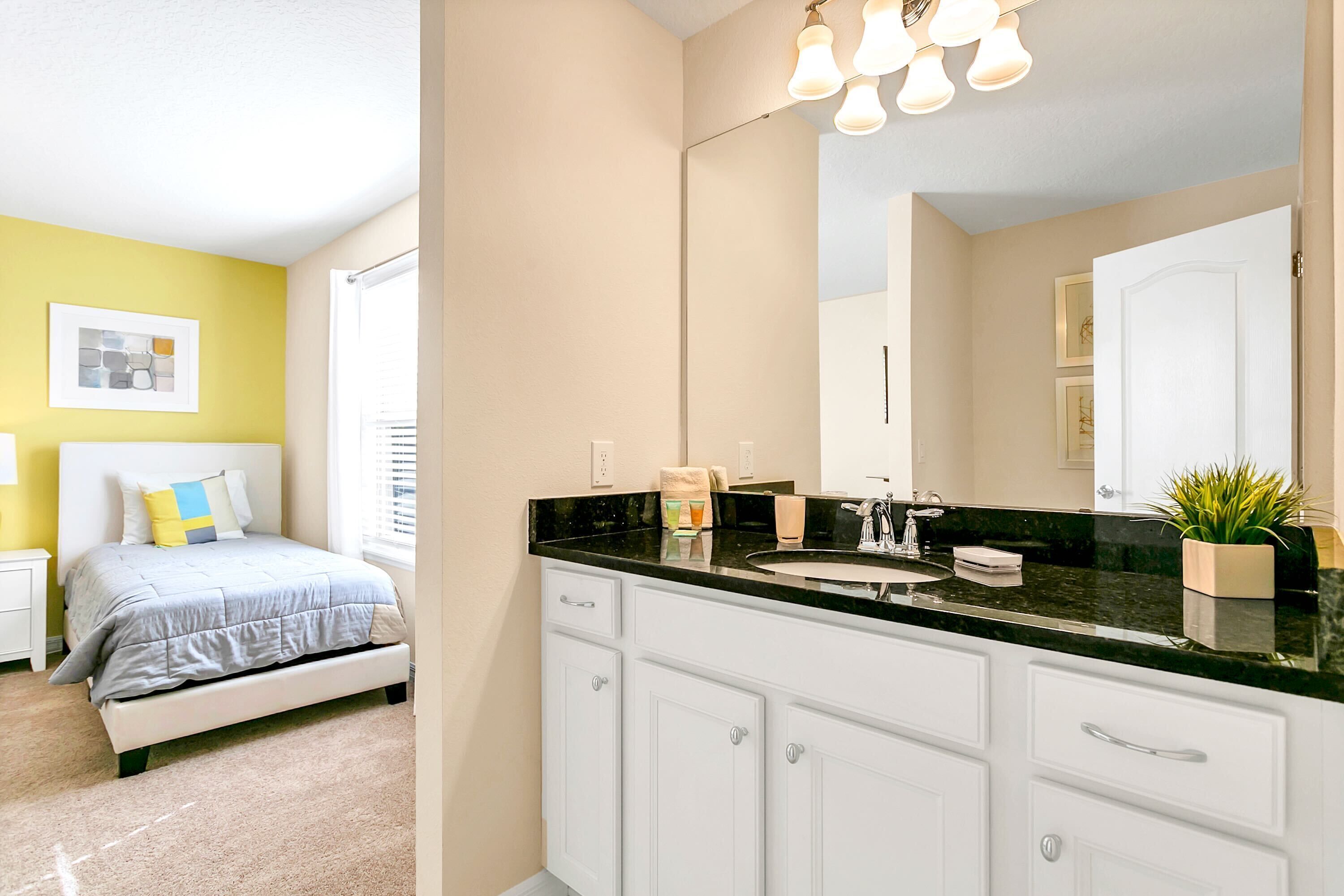 Un dormitorio con cama, mesita de noche y lámpara de noche. La habitación tiene una ventana con persianas, un cuadro en la pared y una lámpara en el techo.