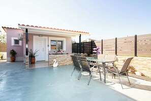 Un patio con una mesa, sillas, una decoración de cisne y una pequeña construcción con puerta y ventana.