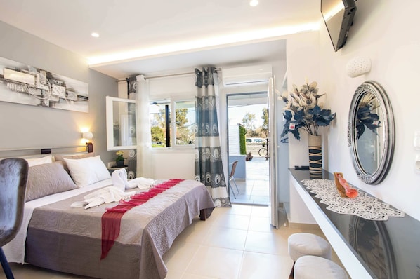 A hotel room with a bed, a desk, a chair, a mirror, and a view of the outdoors.