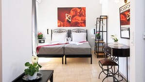 Ein Schlafzimmer mit Doppelbett, Schreibtisch mit Stuhl, einem kleinen Tisch mit Pflanze und einer Wandregal.