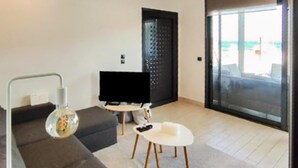 En moderne stue med en grå sofa, et lille hvidt sofabord og et fjernsyn.