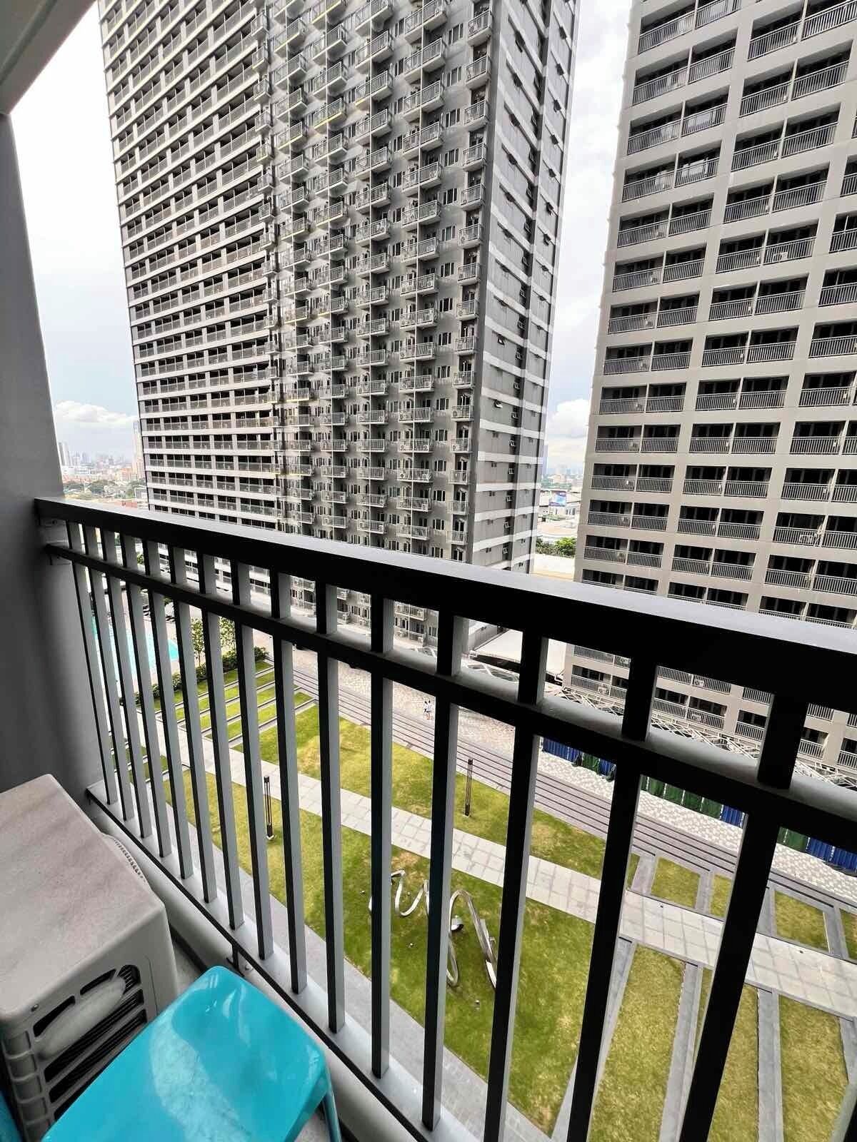 A balcony with a view of high-rise buildings, a grassy area, and a road.