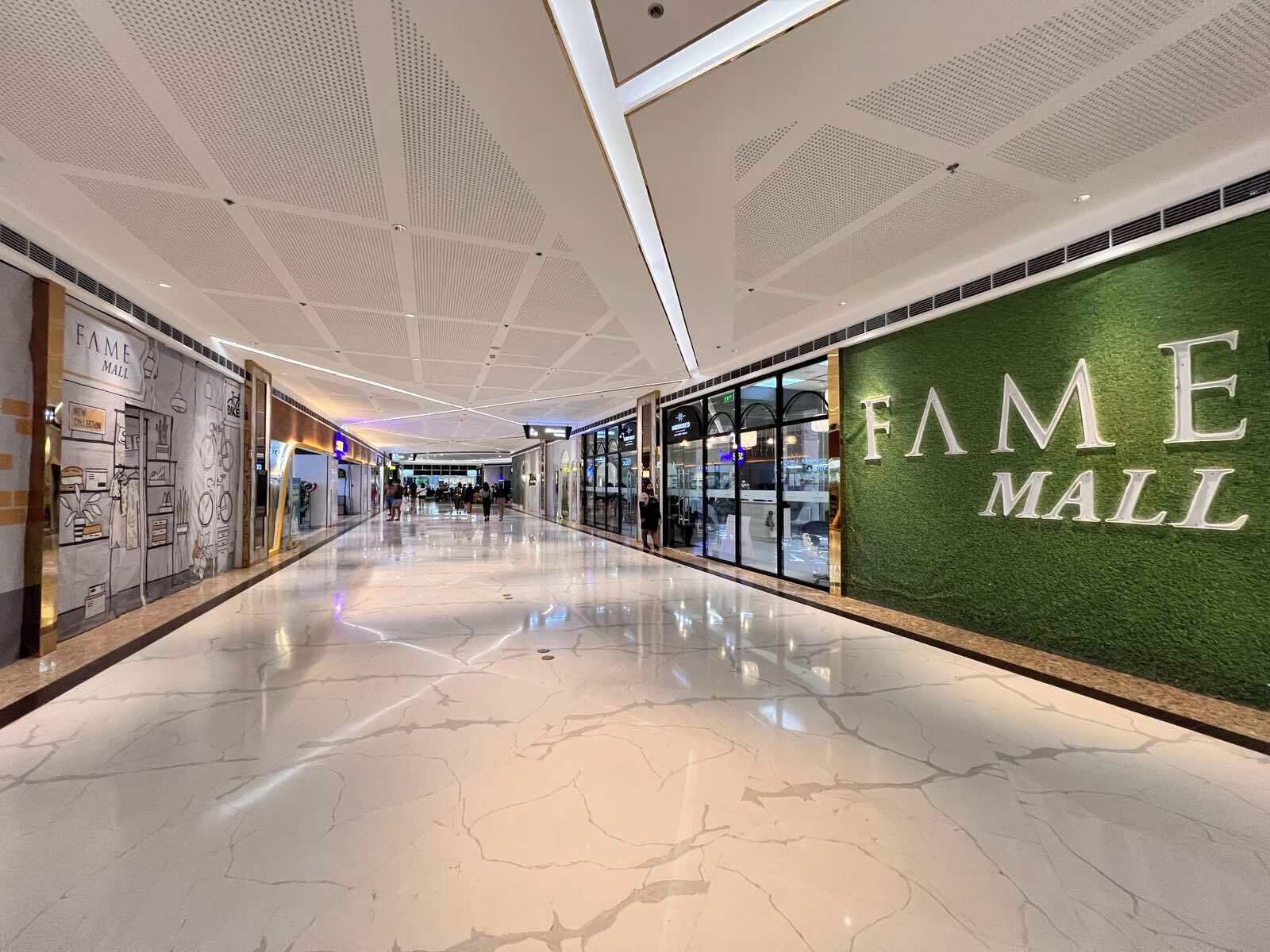 A corridor with a polished marble floor, glass storefronts, and a green wall with 'FAME MALL' signage.