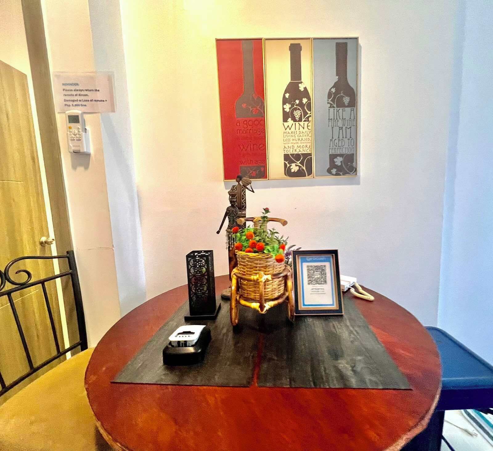 A round table with a framed certificate, a small black object, a decorative basket with flowers, and a QR code.