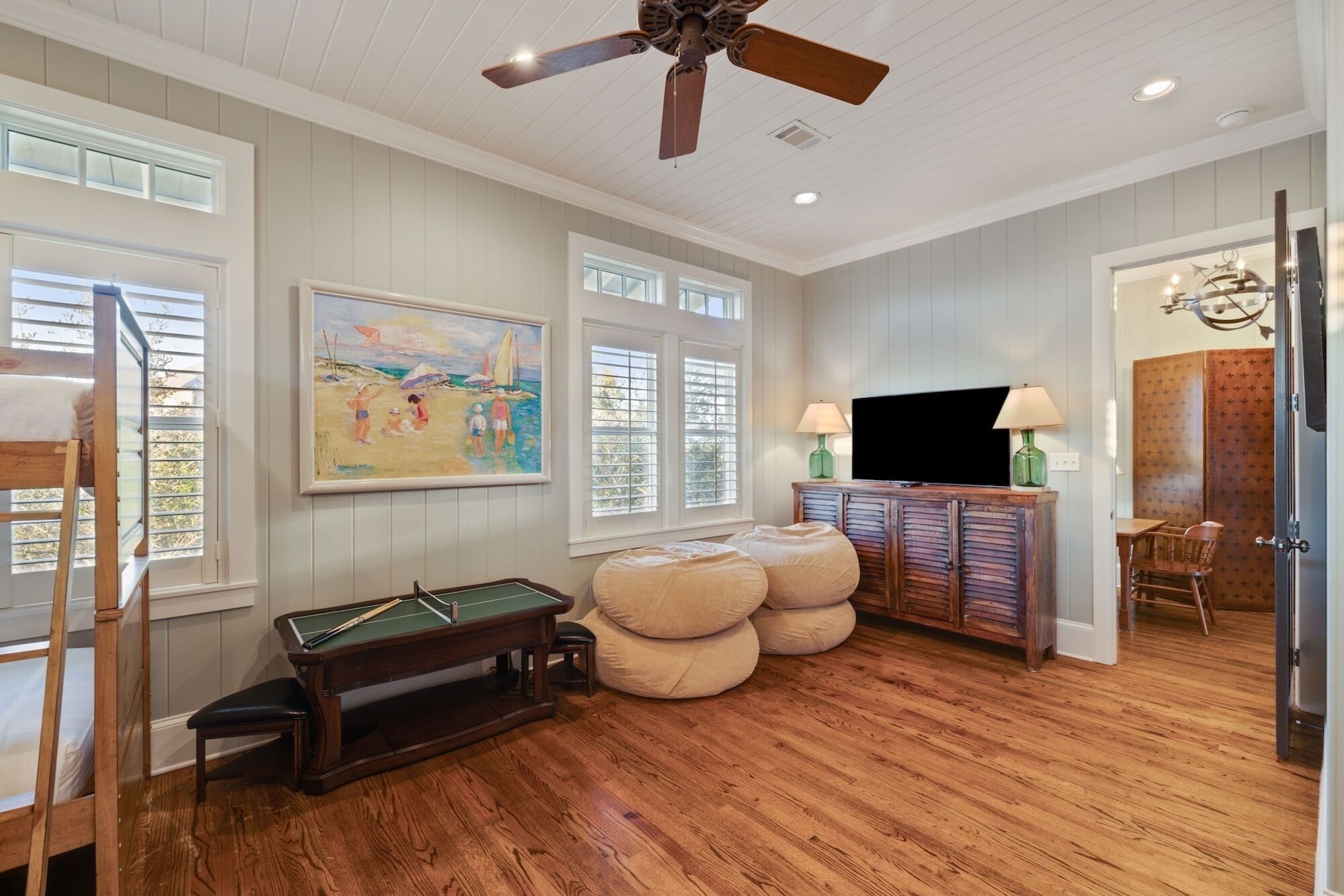 A living room with a pool table, a ceiling fan, and a painting of a beach scene.