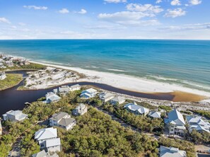 Vue aérienne d’une zone résidentielle côtière, avec des maisons, une plage et une rivière.